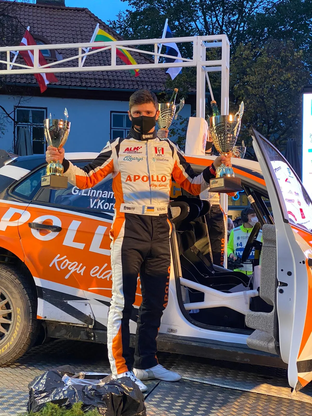 Podiumceremonie met bekers bij de Saaremaa-rally, rallyauto op de achtergrond